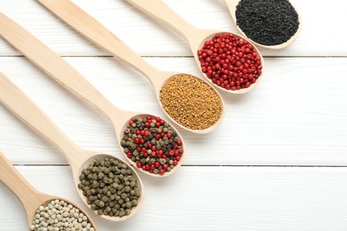 Photo of Different aromatic spices in spoons on white wooden table, flat lay. Space for text