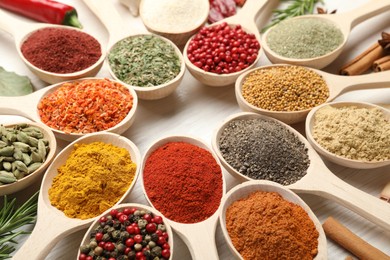 Photo of Different aromatic spices in spoons on white wooden table, closeup