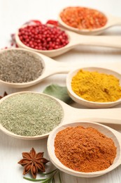 Photo of Different aromatic spices in spoons on white wooden table, closeup