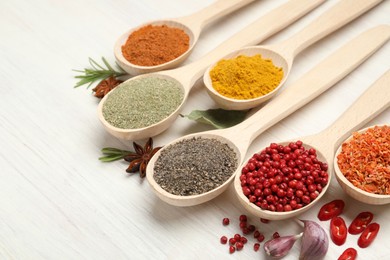 Photo of Different aromatic spices in spoons on white wooden table, closeup