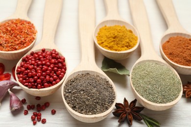Photo of Different aromatic spices in spoons on white wooden table, closeup