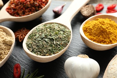 Photo of Different aromatic spices in spoons on black table, closeup