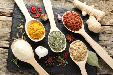 Photo of Different aromatic spices in spoons on wooden table, flat lay