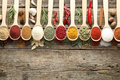 Photo of Different aromatic spices in spoons on wooden table, flat lay. Space for text