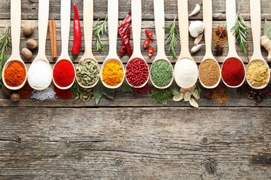 Photo of Different aromatic spices in spoons on wooden table, flat lay. Space for text