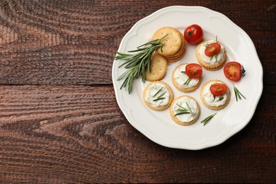 Photo of Tasty crackers with cream cheese, rosemary and tomatoes on wooden table, top view. Space for text
