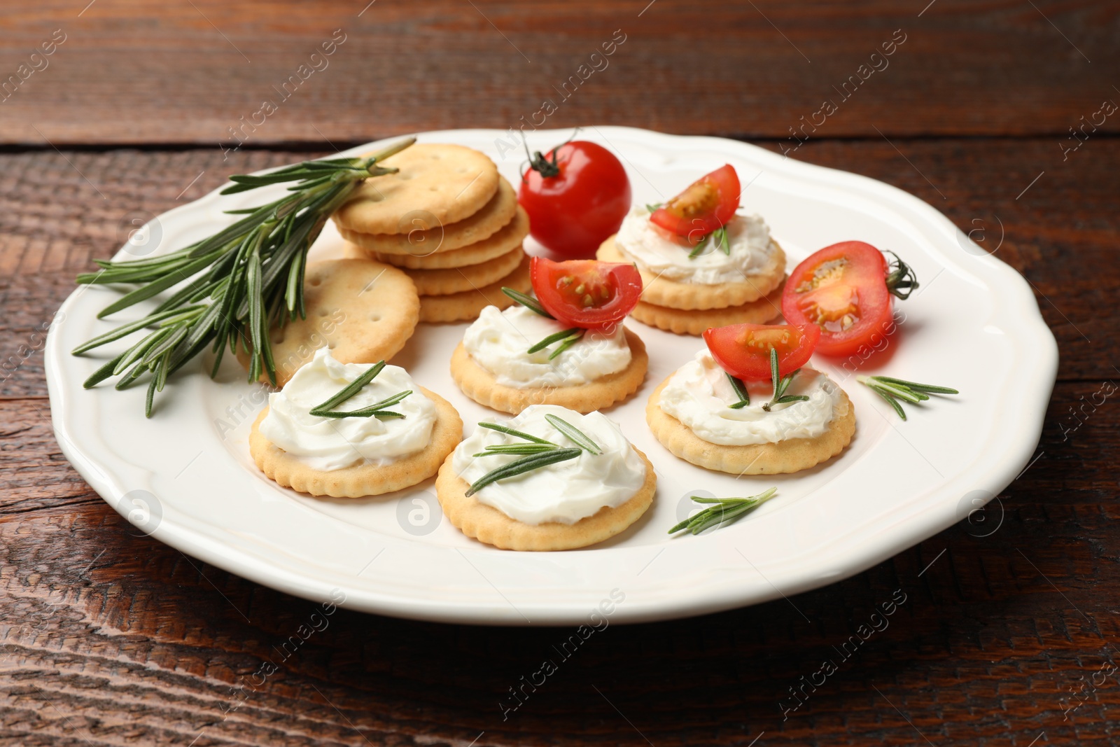 Tasty crackers with cream cheese, rosemary and tomatoes on wooden table, closeup Photo of Tasty crackers with cream cheese, rosemary and tomatoes on wooden table, closeup