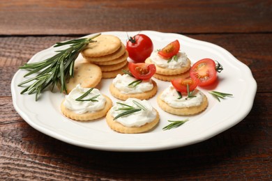 Photo of Tasty crackers with cream cheese, rosemary and tomatoes on wooden table, closeup
