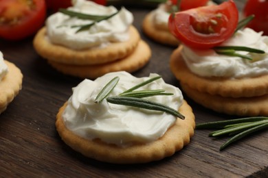 Photo of Tasty crackers with cream cheese, rosemary and tomatoes on wooden table, closeup