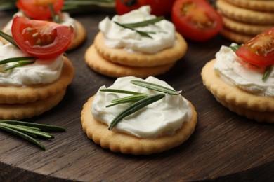 Photo of Tasty crackers with cream cheese, rosemary and tomatoes on wooden table, closeup
