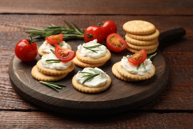 Photo of Tasty crackers with cream cheese, rosemary and tomatoes on wooden table, closeup