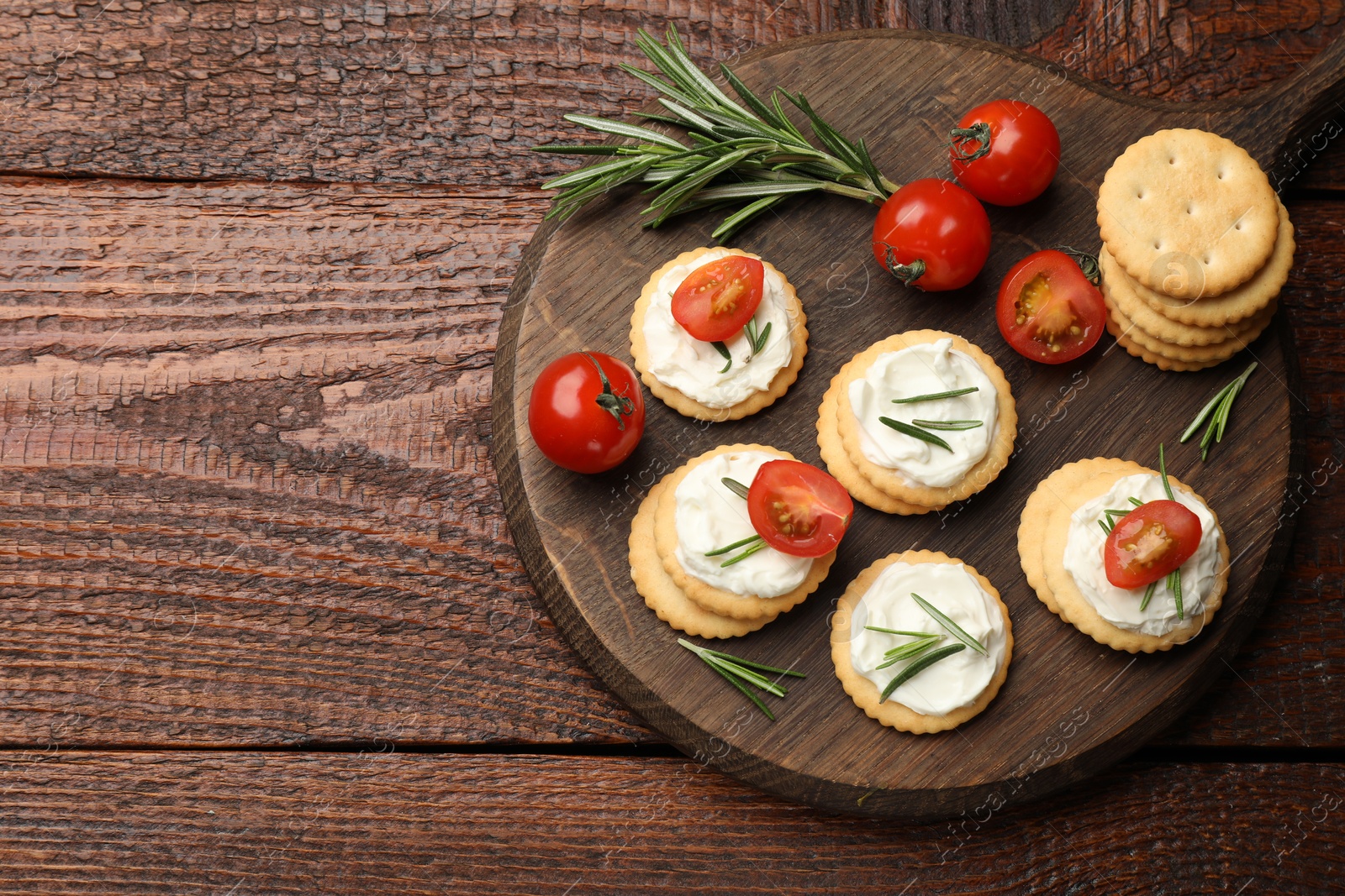 Tasty crackers with cream cheese, rosemary and tomatoes on wooden table, top view. Space for text Photo of Tasty crackers with cream cheese, rosemary and tomatoes on wooden table, top view. Space for text