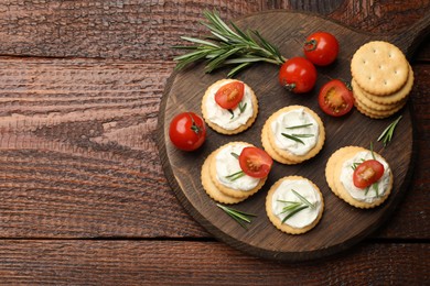 Photo of Tasty crackers with cream cheese, rosemary and tomatoes on wooden table, top view. Space for text