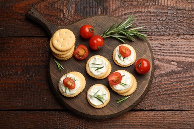 Photo of Tasty crackers with cream cheese, rosemary and tomatoes on wooden table, top view