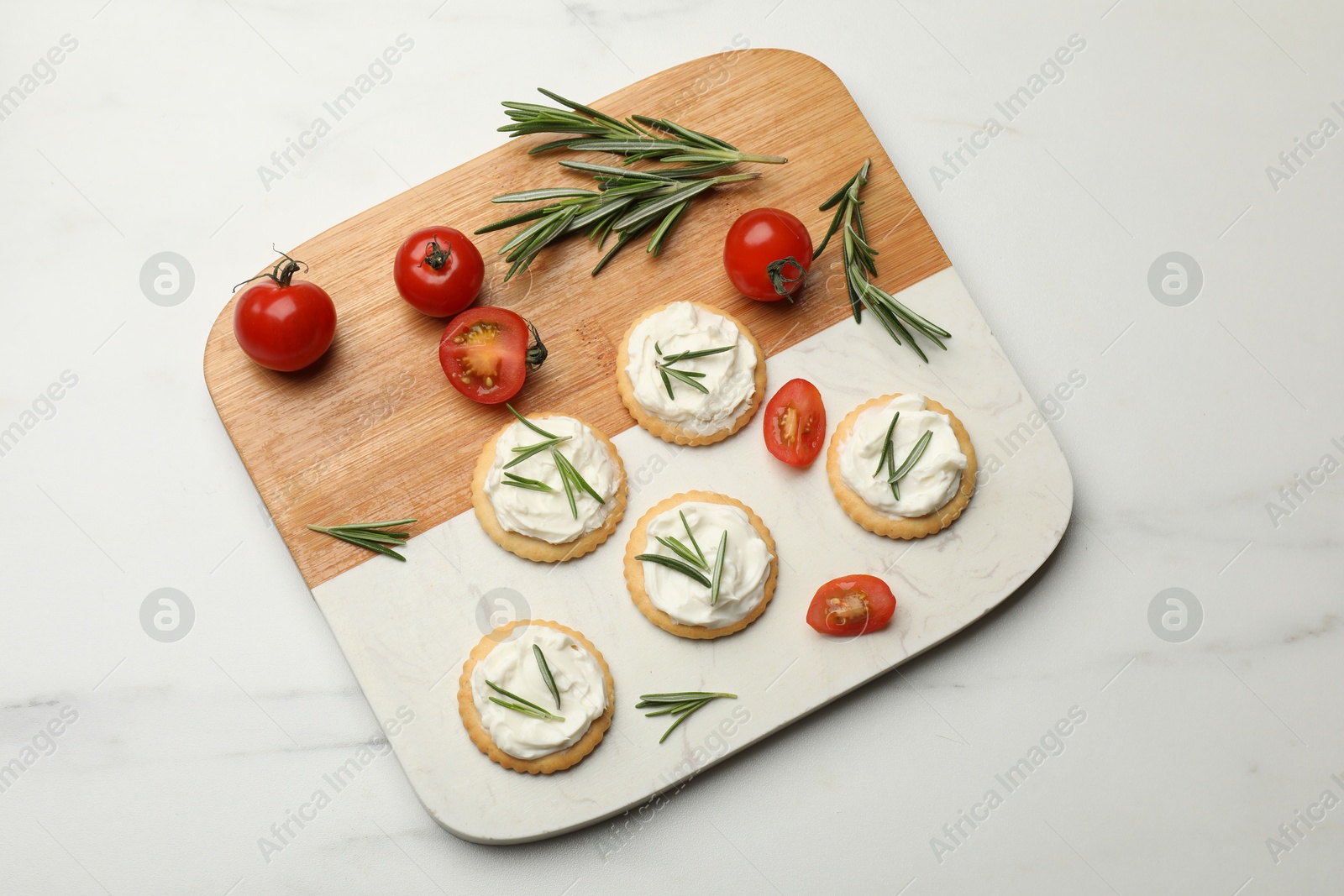 Tasty crackers with cream cheese, rosemary and tomatoes on white table, top view Photo of Tasty crackers with cream cheese, rosemary and tomatoes on white table, top view