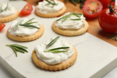 Photo of Tasty crackers with cream cheese, rosemary and tomatoes on white table, closeup