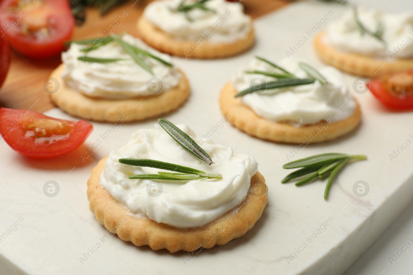 Photo of Tasty crackers with cream cheese, rosemary and tomatoes on white table, closeup