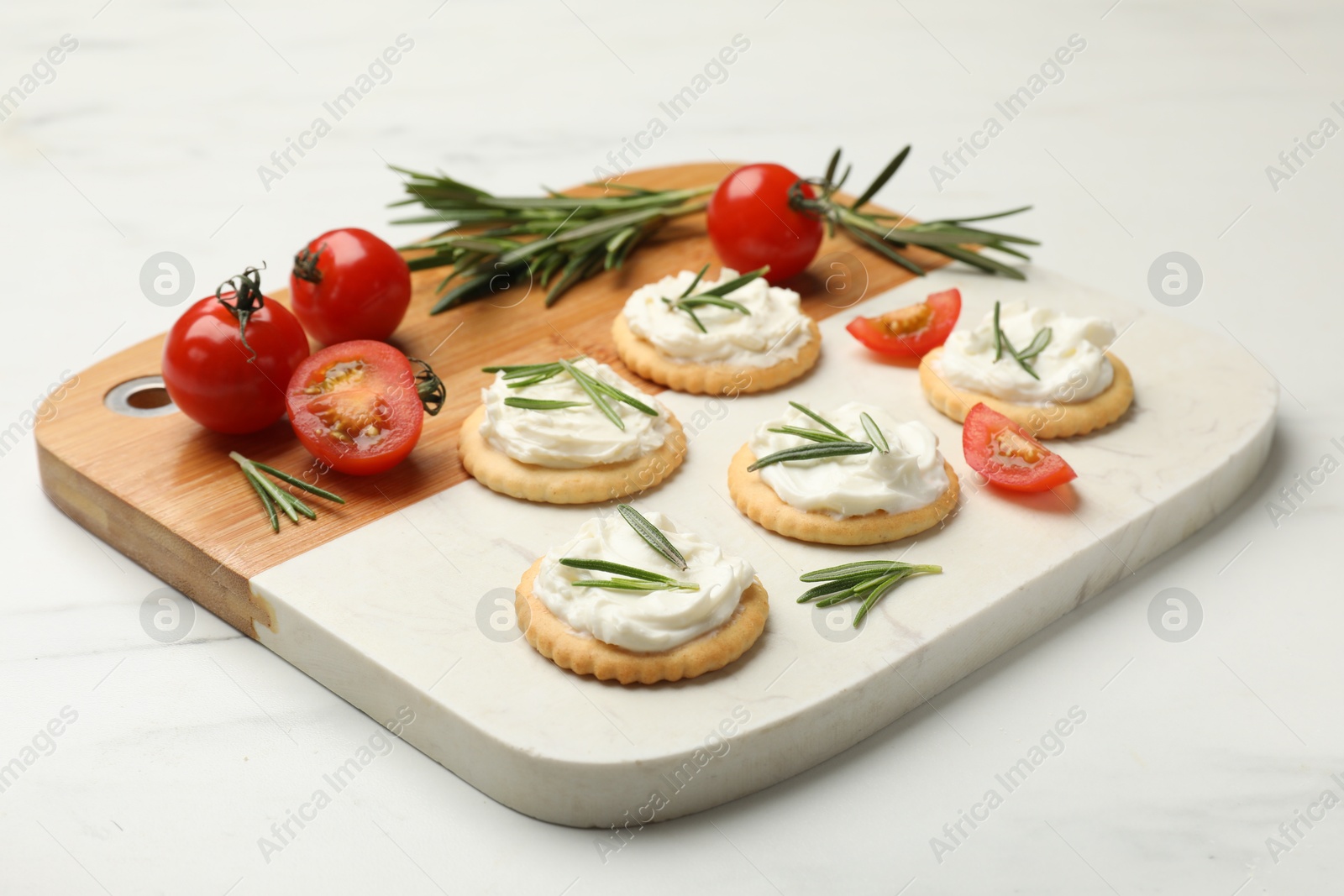 Photo of Tasty crackers with cream cheese, rosemary and tomatoes on white table, closeup