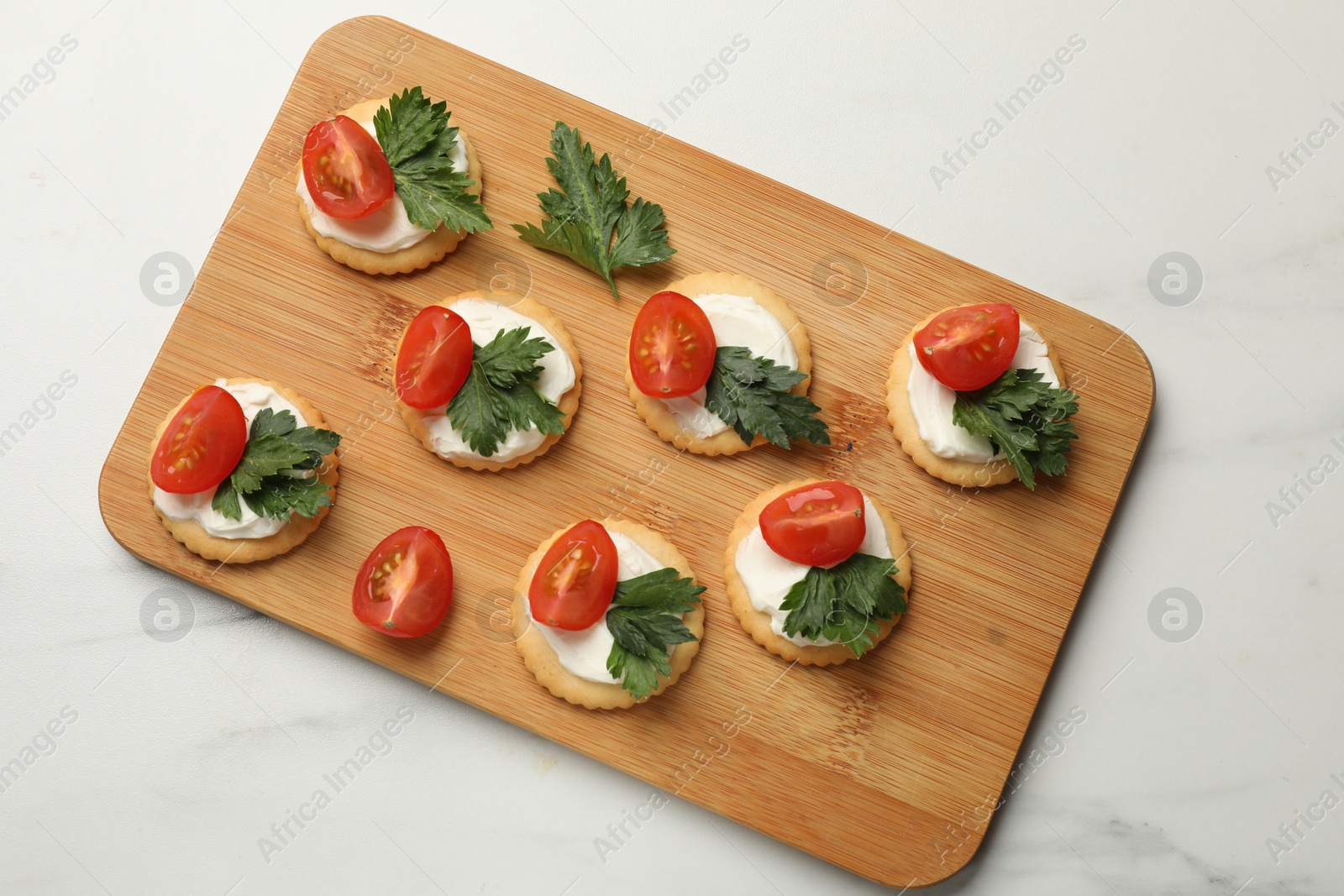 Photo of Tasty crackers with cream cheese, tomatoes and parsley on white table, top view