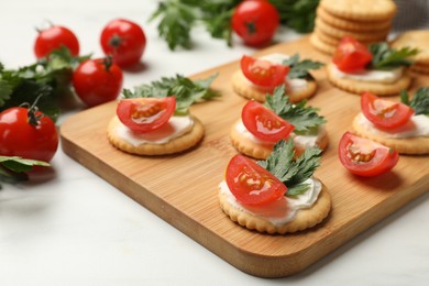 Photo of Tasty crackers with cream cheese, tomatoes and parsley on white table, closeup