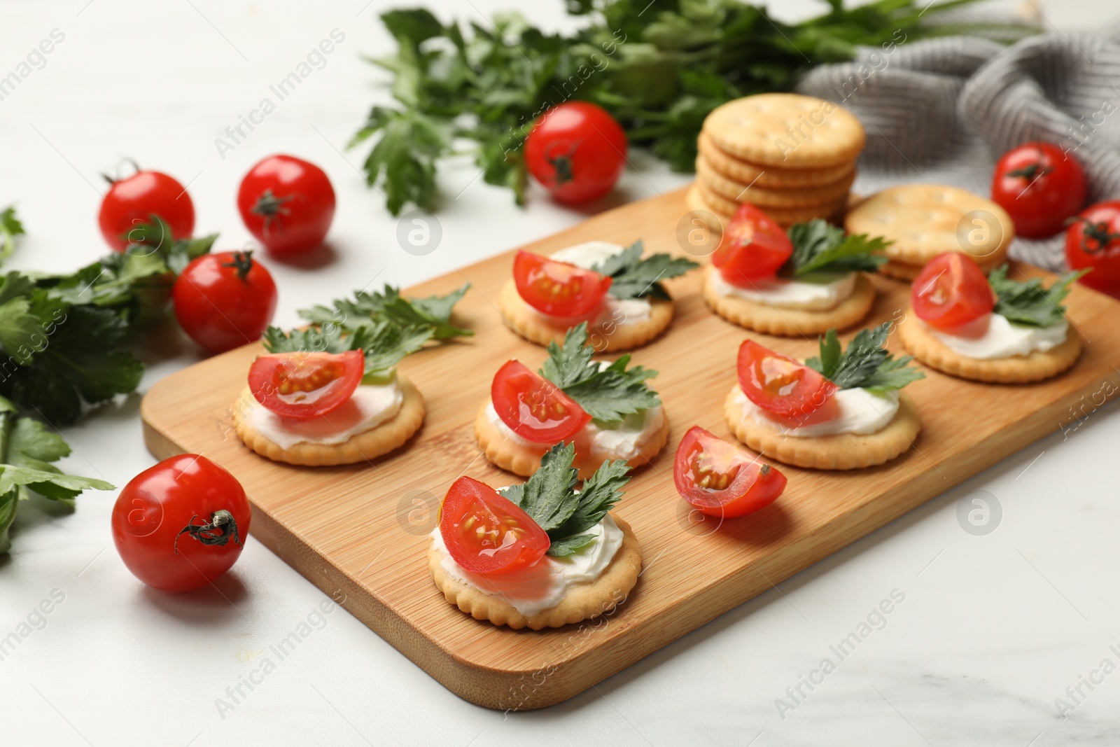 Photo of Tasty crackers with cream cheese, tomatoes and parsley on white table, closeup