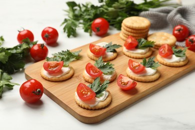 Photo of Tasty crackers with cream cheese, tomatoes and parsley on white table, closeup