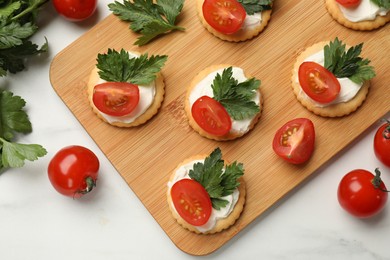 Photo of Tasty crackers with cream cheese, tomatoes and parsley on white table, flat lay