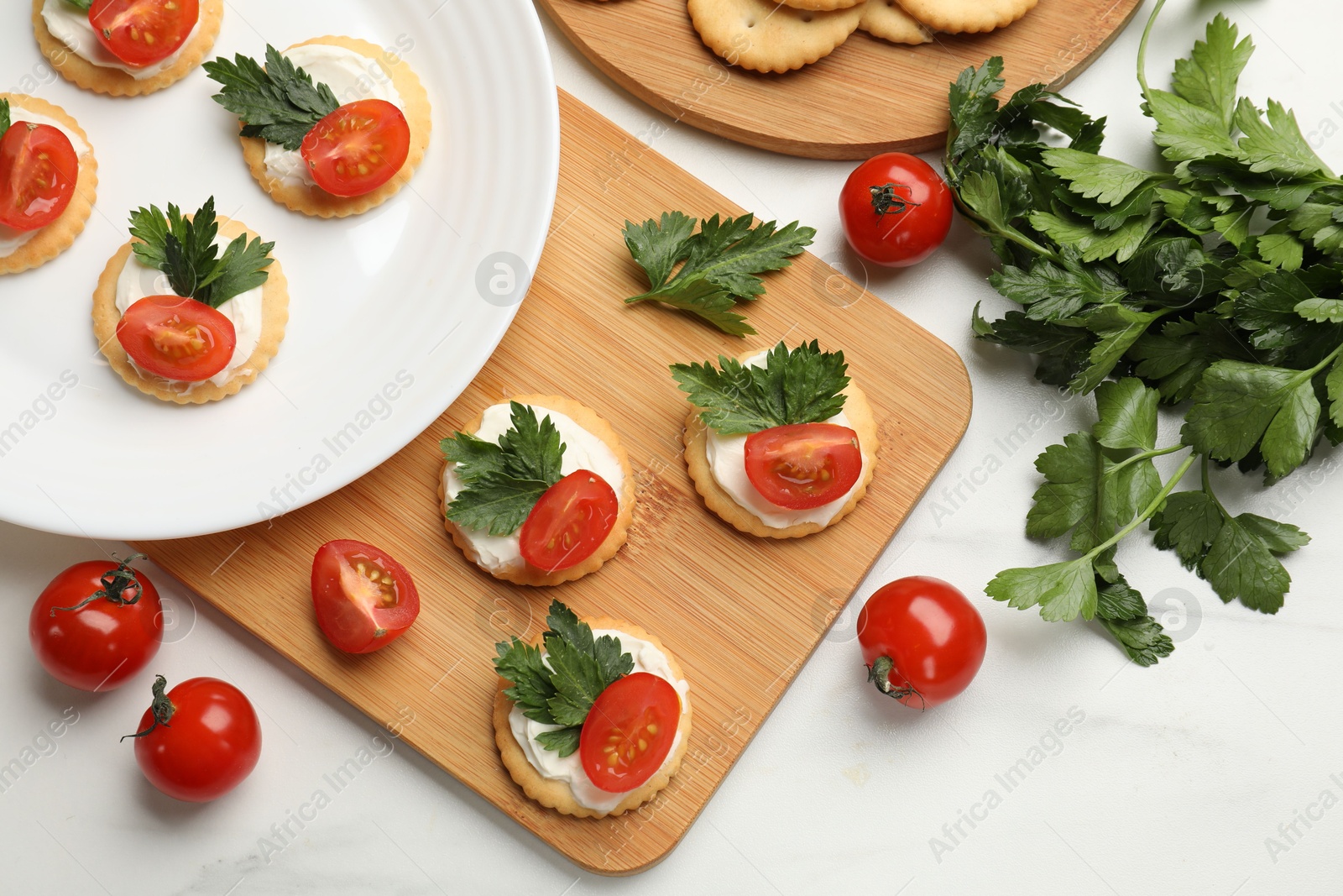Photo of Tasty crackers with cream cheese, tomatoes and parsley on white table, flat lay