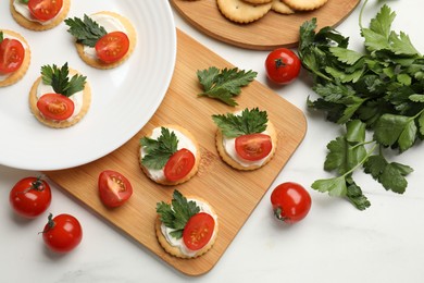 Photo of Tasty crackers with cream cheese, tomatoes and parsley on white table, flat lay