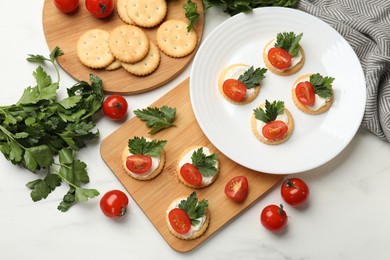 Photo of Tasty crackers with cream cheese, tomatoes and parsley on white table, flat lay