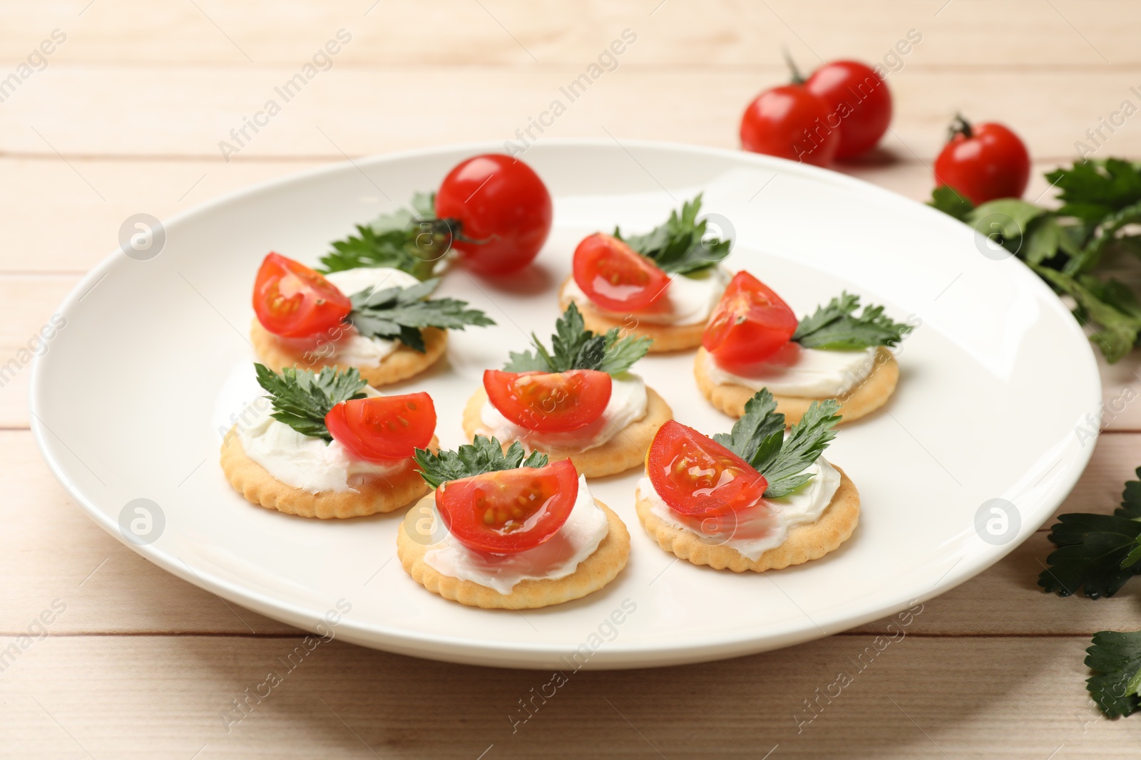 Photo of Tasty crackers with cream cheese, tomatoes and parsley on white wooden table, closeup