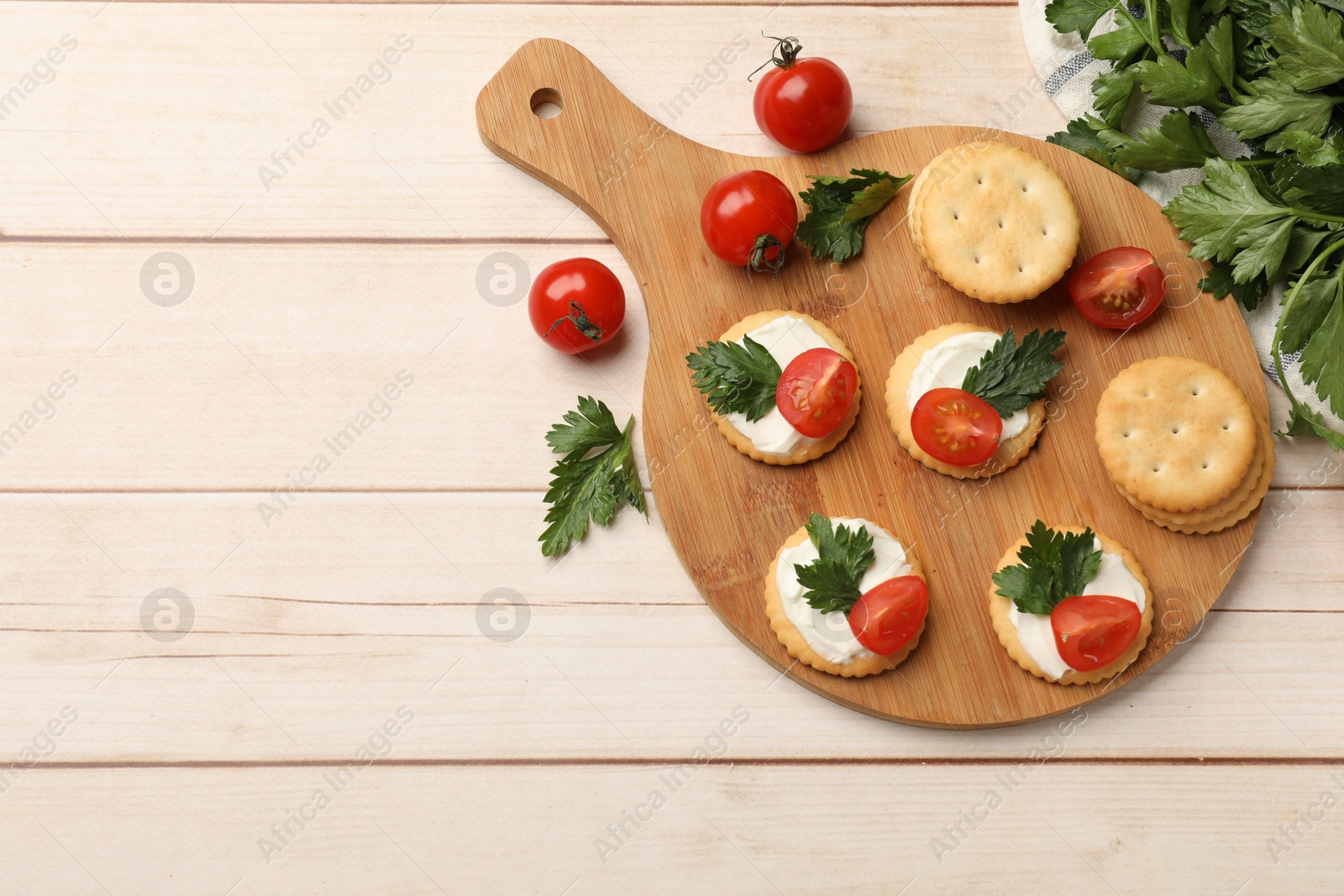 Photo of Tasty crackers with cream cheese, tomatoes and parsley on white wooden table, flat lay. Space for text