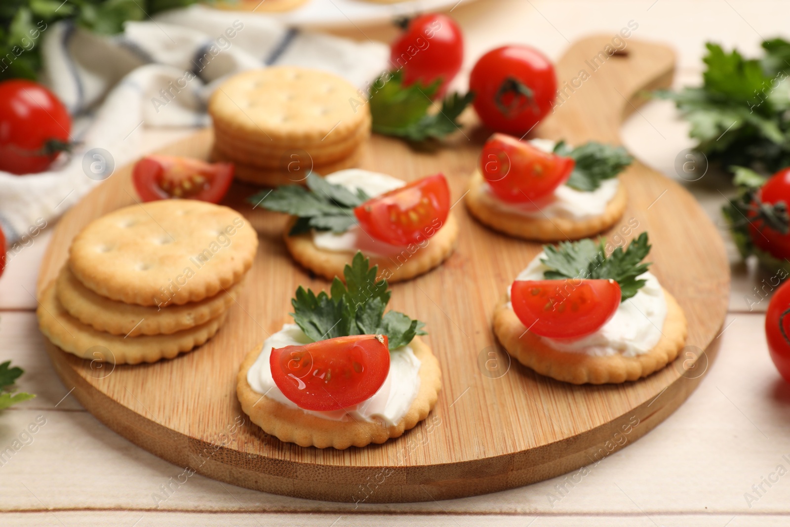 Photo of Tasty crackers with cream cheese, tomatoes and parsley on white wooden table, closeup