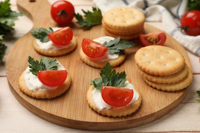 Photo of Tasty crackers with cream cheese, tomatoes and parsley on white wooden table, closeup