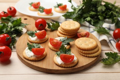 Photo of Tasty crackers with cream cheese, tomatoes and parsley on white wooden table, closeup
