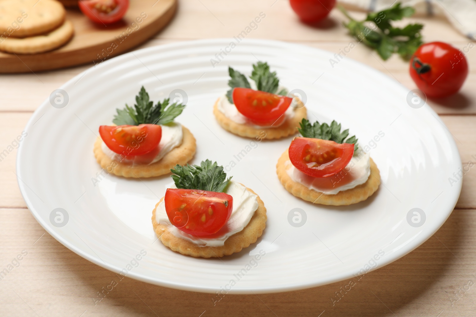 Photo of Tasty crackers with cream cheese, tomatoes and parsley on white wooden table, closeup