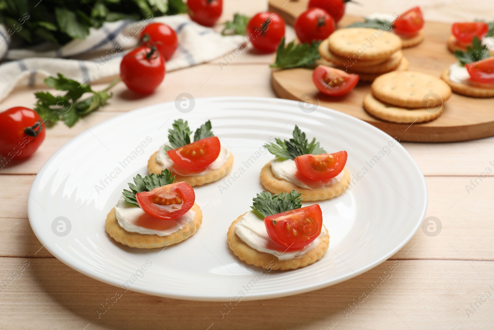 Photo of Tasty crackers with cream cheese, tomatoes and parsley on white wooden table, closeup