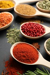 Photo of Different aromatic spices in spoons on black table, closeup