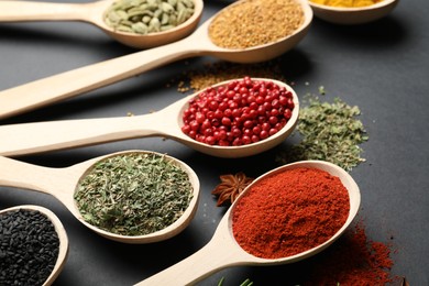 Photo of Different aromatic spices in spoons on black table, closeup
