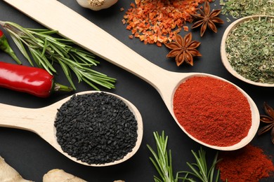 Photo of Different aromatic spices in spoons on black table, flat lay