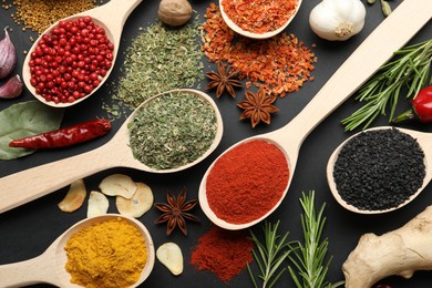 Photo of Different aromatic spices in spoons on black table, flat lay