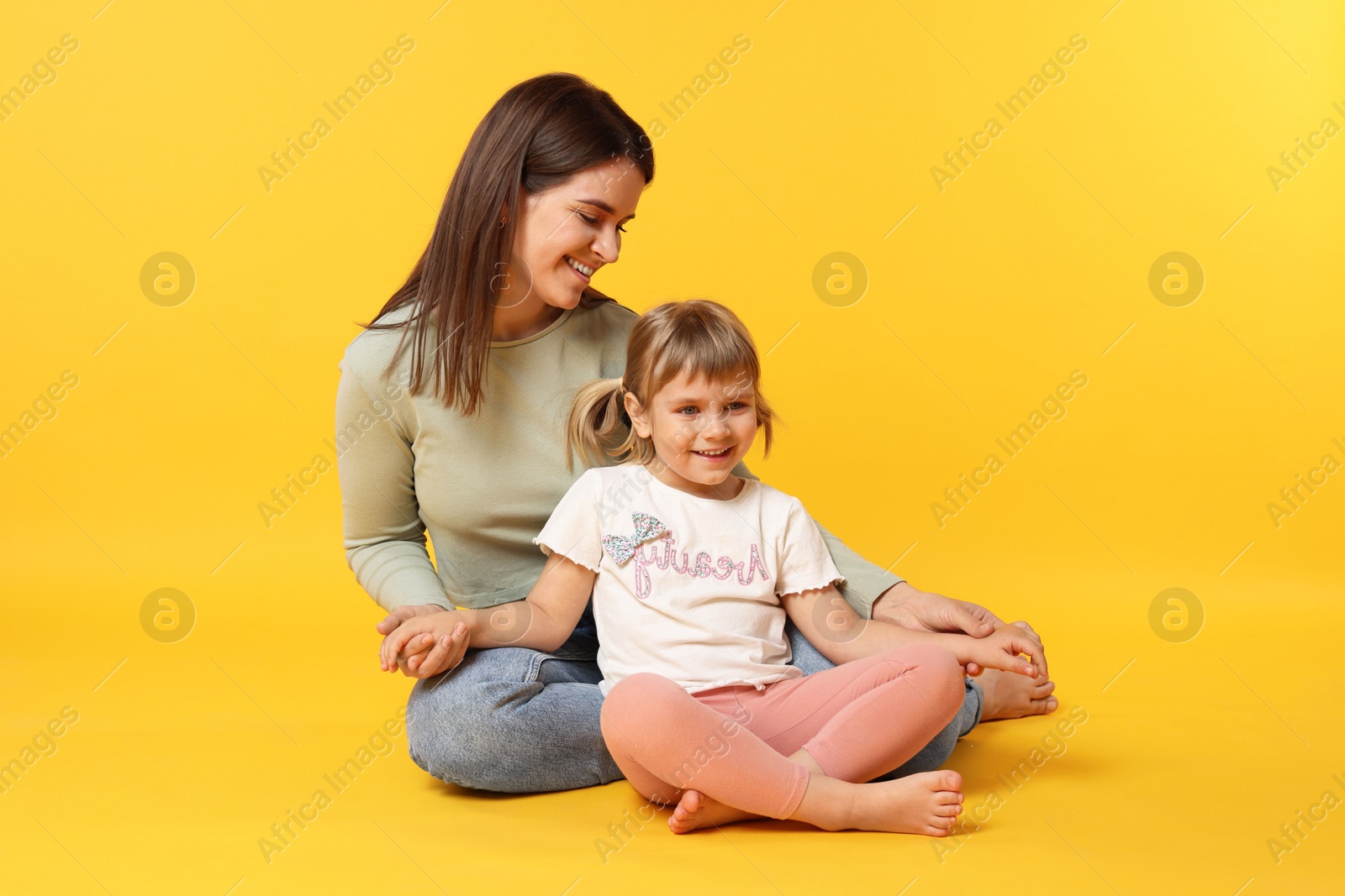 Happy mother and her cute daughter on orange background Photo of Happy mother and her cute daughter on orange background