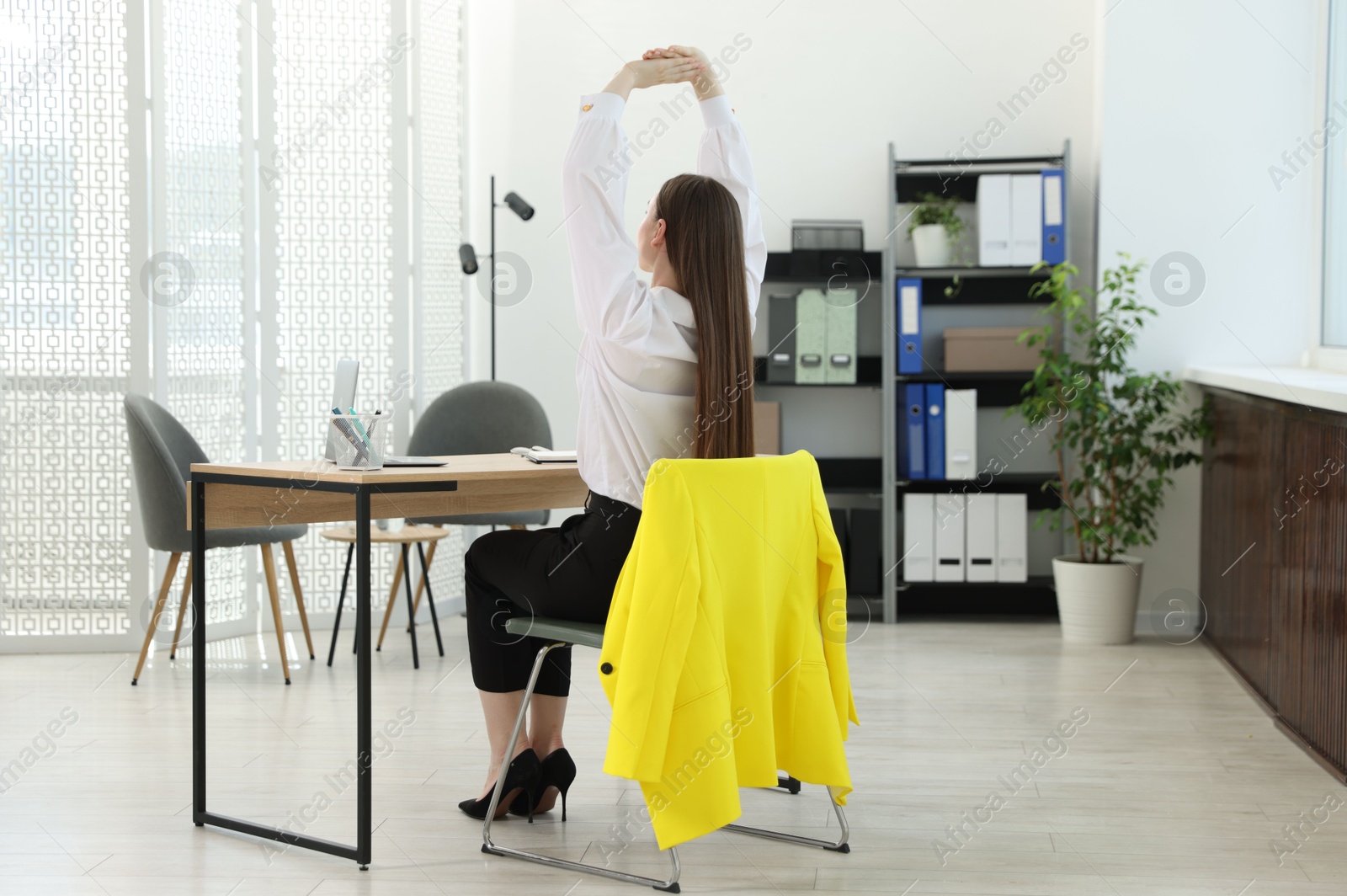 Young woman stretching on chair in office Photo of Young woman stretching on chair in office