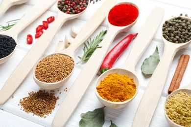 Photo of Different aromatic spices in spoons on white wooden table, closeup