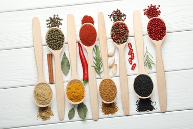 Photo of Different aromatic spices in spoons on white wooden table, flat lay