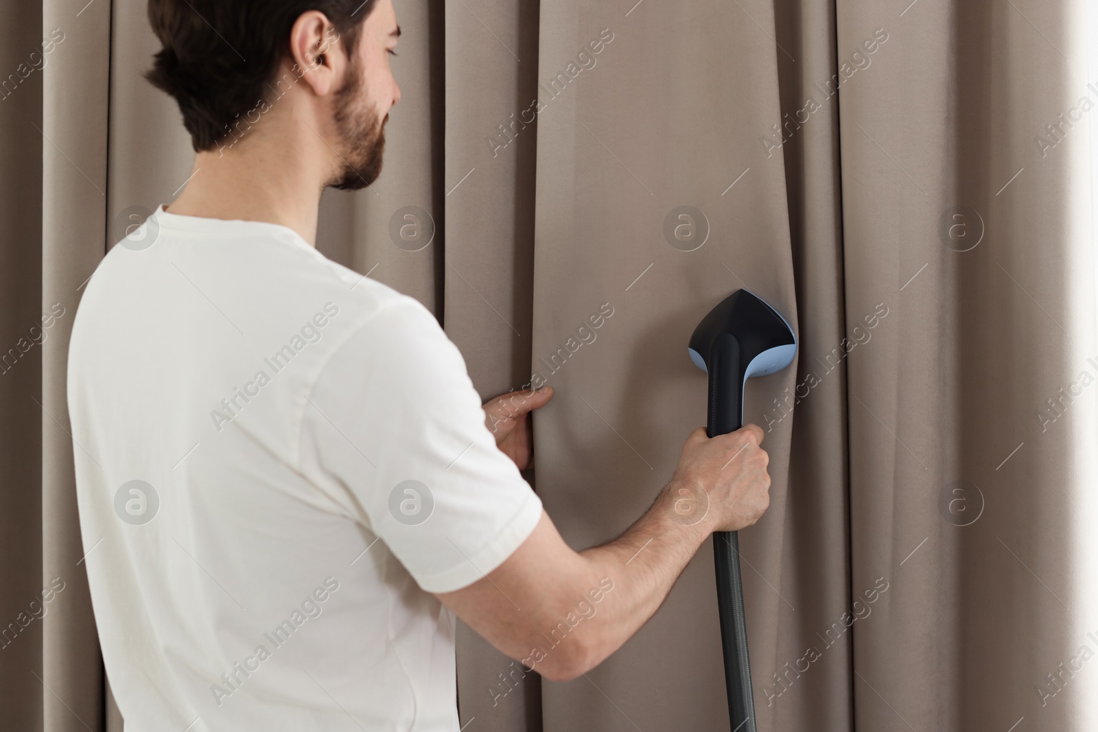 Man steaming curtains with stand steamer at home Photo of Man steaming curtains with stand steamer at home