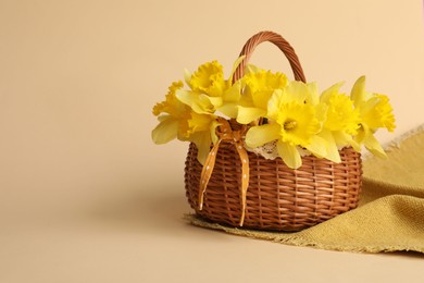 Photo of Beautiful daffodils in basket on beige background. Space for text