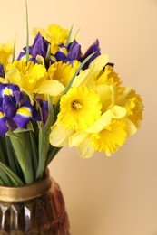 Photo of Bouquet of beautiful daffodils and irises in vase on beige background, closeup