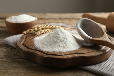 Photo of Wheat flour, spikelets and spoon on wooden table, closeup