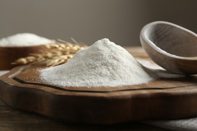 Photo of Wheat flour, spikelets and spoon on wooden table, closeup